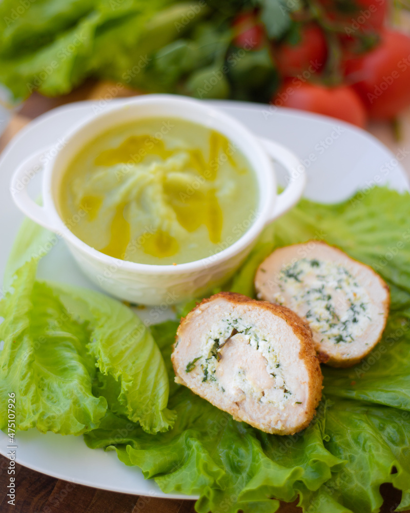 Ricotta cheese mixed with herbs in a chicken roll lies on lettuce leaves and vegetable puree next to it.