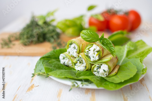 Ricotta cheese mixed with herbs in a zucchini roll lies on lettuce leaves.