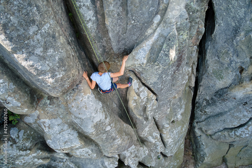 Young child boy climbing steep wall of rocky mountain. Kid climber overcomes challenging route. Engaging in extreme sport concept Young child boy climbing steep wall of rocky mountain. Kid climber overcomes challenging route. Engaging in extreme sport concept