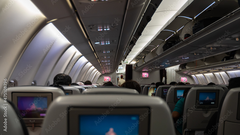 passenger seat, Interior of airplane with passengers sitting on seats and stewardess walking the aisle in background. passenger seat, Interior of airplane with passengers sitting on seats and stewardess walking the aisle in background.