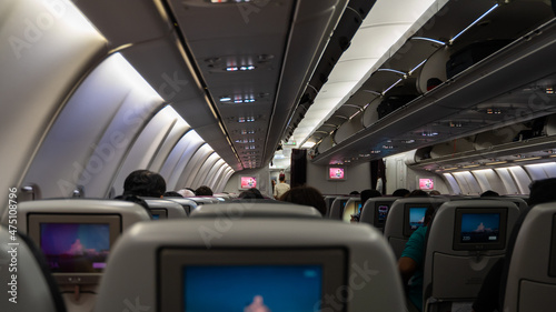 passenger seat, Interior of airplane with passengers sitting on seats and stewardess walking the aisle in background.