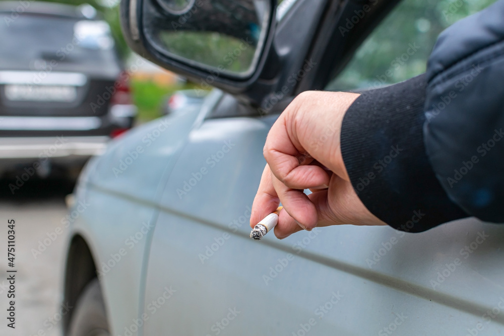 The driver stuck out his hand while holding a cigarette out of the window of his car, enjoying smoking and harming his health