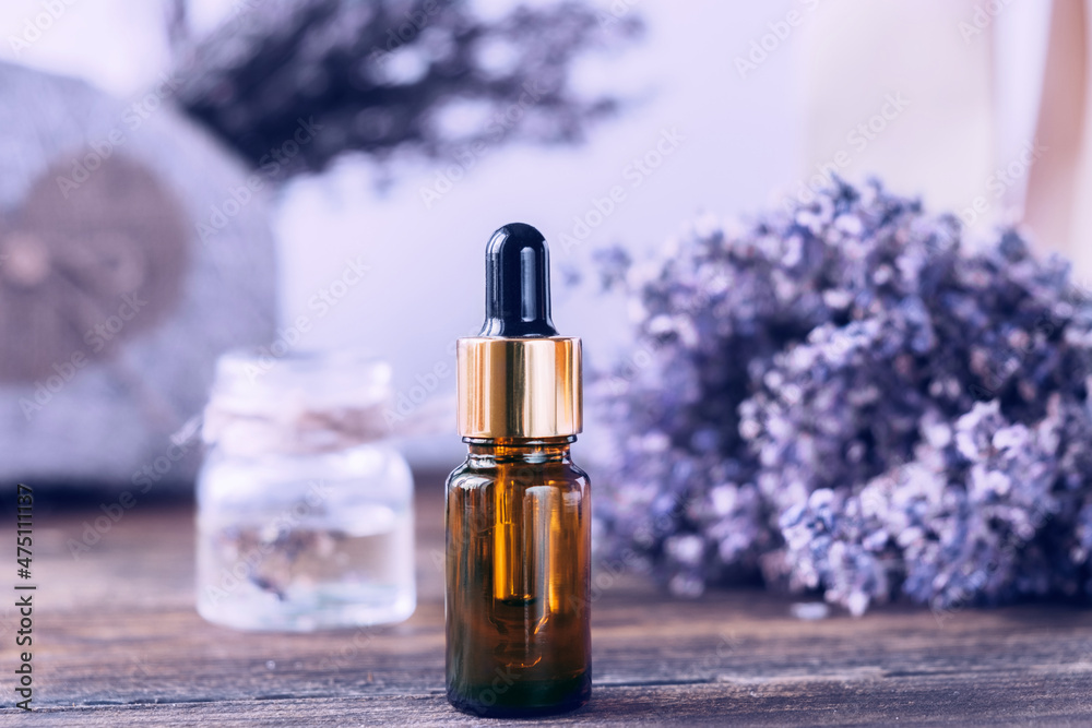 Bottle with lavender essential oil on background of a bouquet of lavender. Purple toning. One bottle on a wooden table Bottle with lavender essential oil on background of a bouquet of lavender. Purple toning. One bottle on a wooden table
