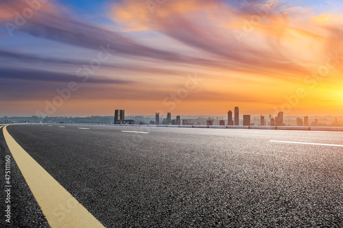 Empty asphalt road with modern city skyline and buildings at sunrise
