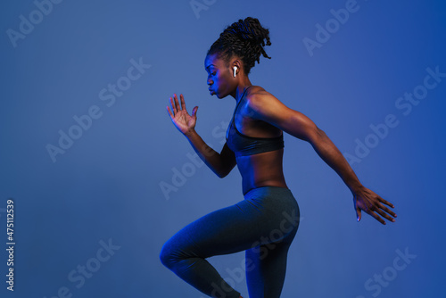 Black sportswoman in earphones doing exercise while working out