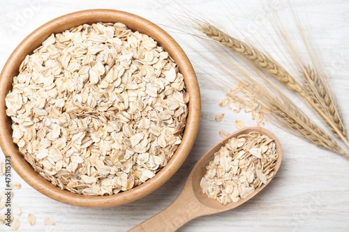 Oatmeal, bowl, spoon and spikelets on white wooden table, flat lay