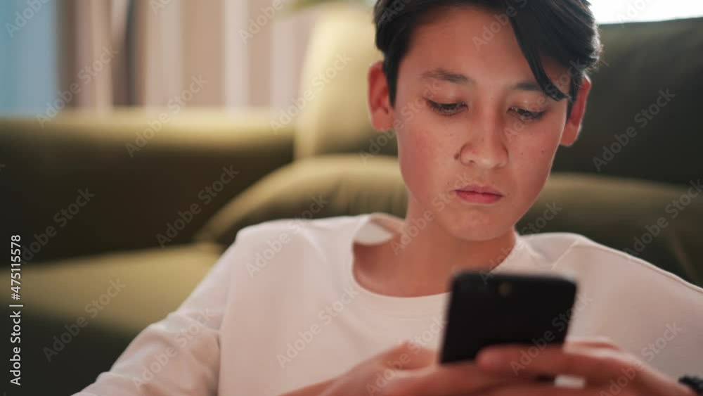 Confident brunet Asian man texting by phone on the sofa Confident brunet Asian man texting by phone on the sofa