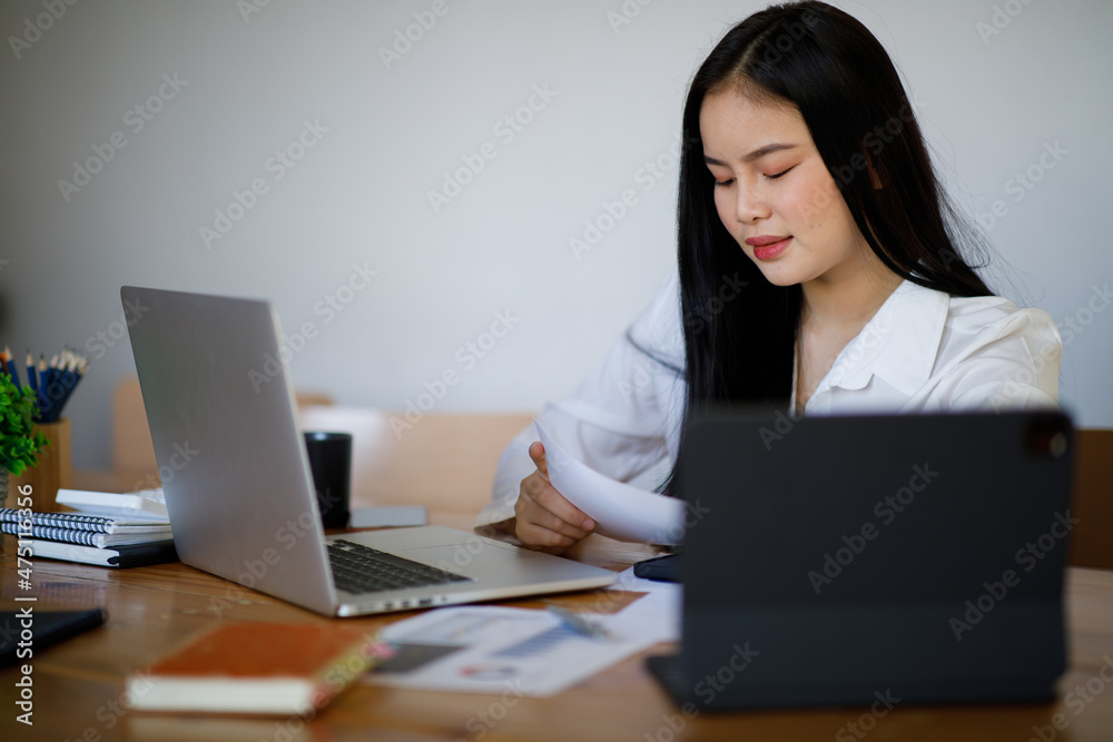 Portrait of Young Asian woman hand freelancer is working her job on computer tablet in modern office. Doing accounting analysis report real estate investment data, Financial and tax systems concept. Portrait of Young Asian woman hand freelancer is working her job on computer tablet in modern office. Doing accounting analysis report real estate investment data, Financial and tax systems concept.