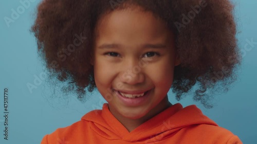Close up of adorable African American girl showing agreement emotion by shaking her head positively on blue background. Kid says 'yes'.