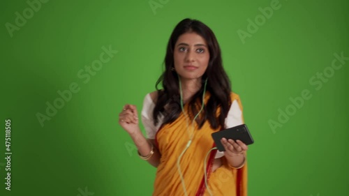 Happy traditional Indian woman listening music in headphones and dancing in the green studio photo