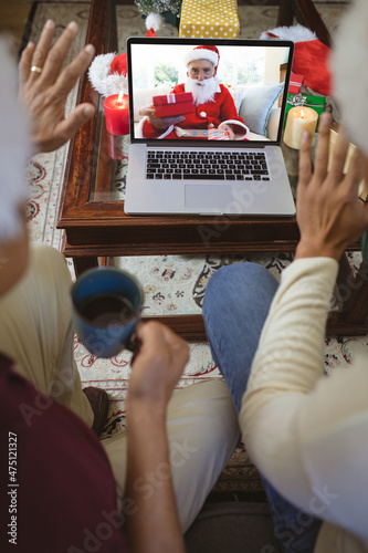 Two waving men making laptop christmas group video call with senior caucasian man in santa costume