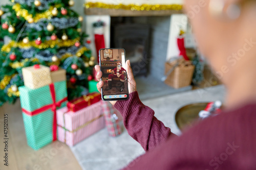 Woman making smartphone christmas video call with santa claus in face mask