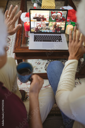 Two waving men making laptop christmas group video call with waving family and friends