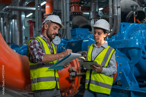 workers in factory. Two worker discuss job in plant room. worker co-worker on water pump on background.