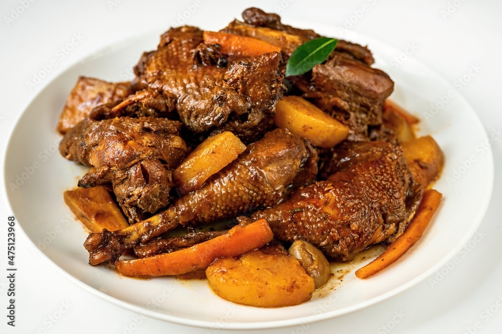 Many pieces of baked hen with carrot, pear and spices on plate.