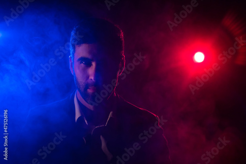 Photo of man looking at camera on dark background with pink and blue lights.