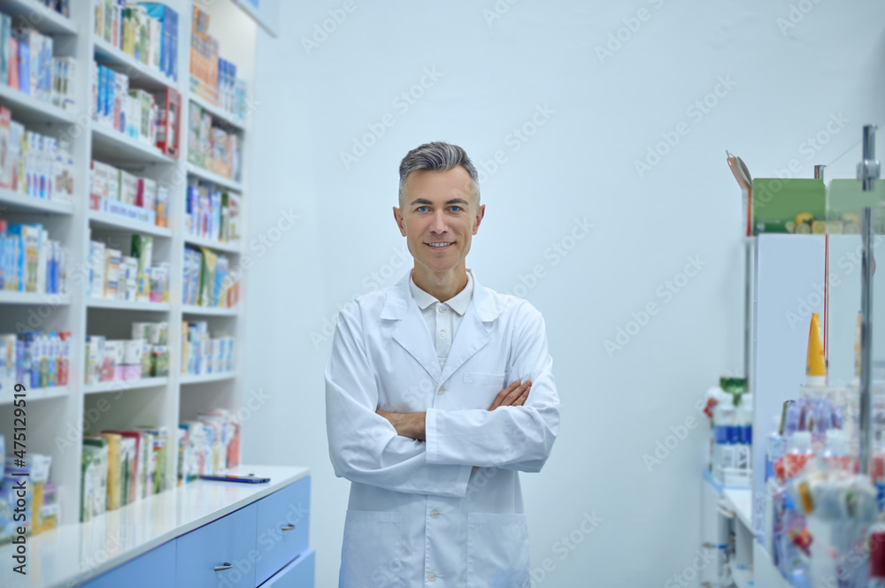 Man in a lab coat standing near the shelves with medicines