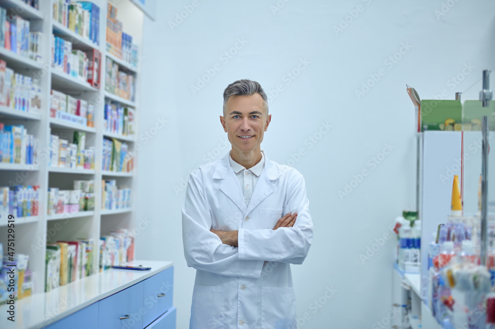 Man in a lab coat standing near the shelves with medicines Man in a lab coat standing near the shelves with medicines