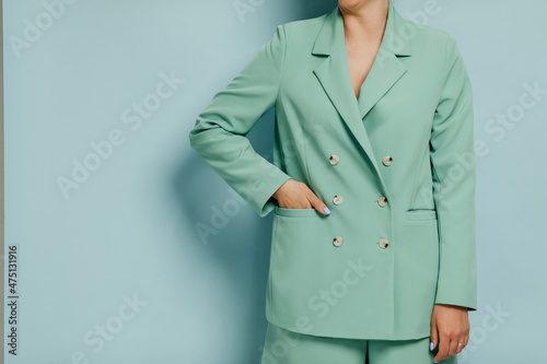 Happy smiling female model wearing a cyan business suit in front of a blue wall