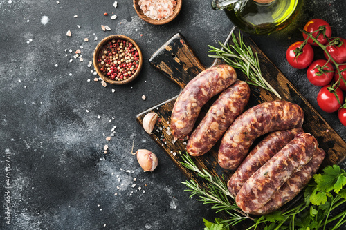 Raw sausages or bratwurst and ingredients for cooking on dark stone background. Top view with copy space.