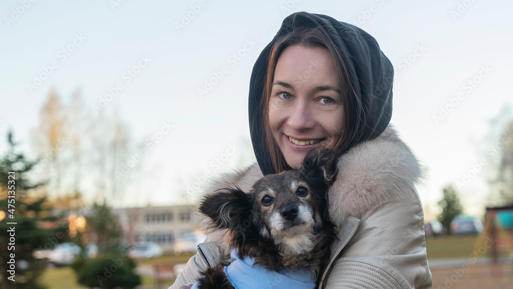 Obraz premium Beautiful girl hugs cute little dog after visits vet. A girl walks on the street with a small dog after surgery.
