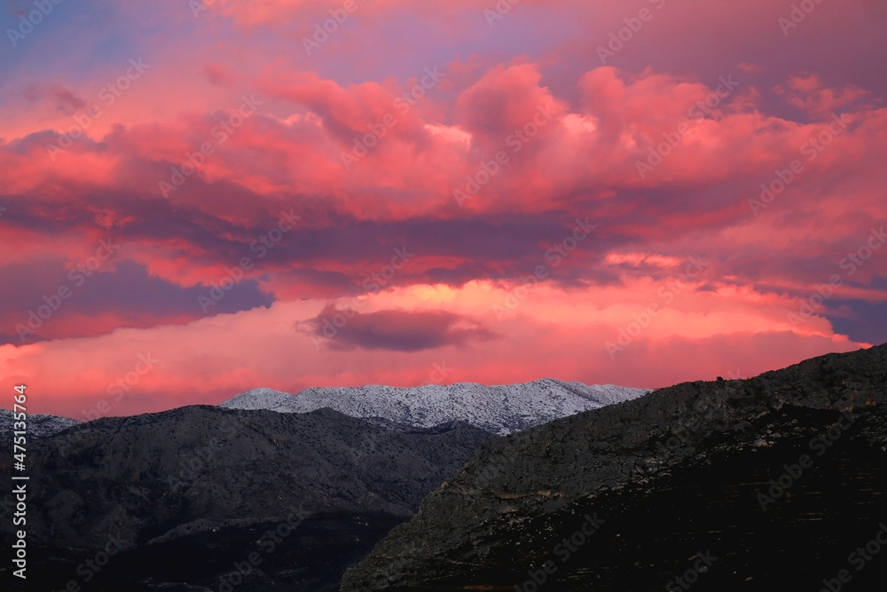 Mountain peaks covered in snow and pink clouds in the sky. Beautiful winter sunset in Croatia.