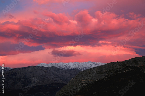 Mountain peaks covered in snow and pink clouds in the sky. Beautiful winter sunset in Croatia.