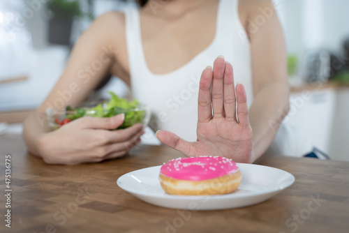 Woman on dieting for good health concept. Close up female using hand push out her favourite donut and choose salad vegetables for good health.