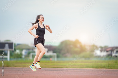 A mature Asian woman athlete runner jogging in city stadium in the sunny morning to keep fitness and healthy lifestyle. Active healthy runner jogging outdoor