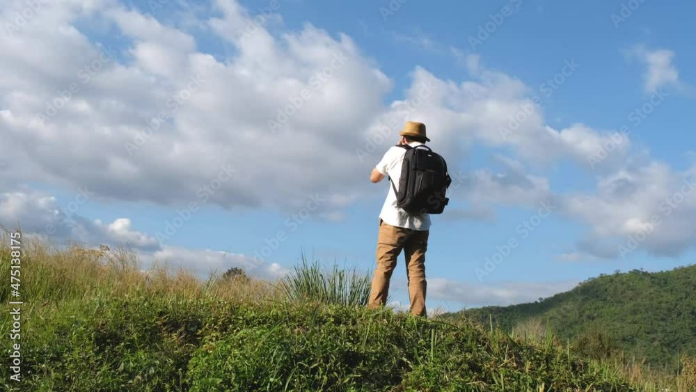 Asian male tourist wearing a white shirt and brown pants with a backpack is taking pictures on the top of a mountain. Asian male tourist wearing a white shirt and brown pants with a backpack is taking pictures on the top of a mountain.