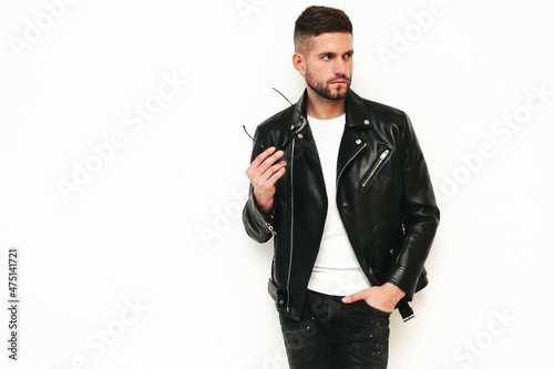 Portrait of handsome confident model. Sexy stylish man dressed in biker leather jacket and black jeans. Fashion hipster male isolated on white in studio