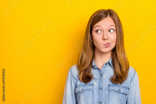Photo of unsure little blond girl look empty space wear jeans shirt isolated on vibrant yellow color background
