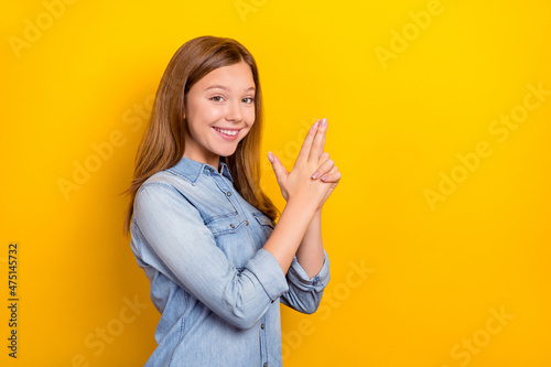 Photo of optimistic small blond girl hands gun wear jeans outfit isolated on vivid yellow color background