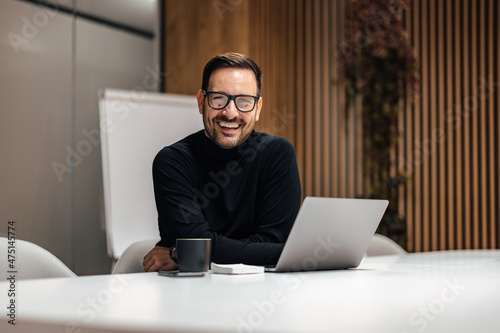 Portrait of smiling caucasian man using his laptop in office. photo