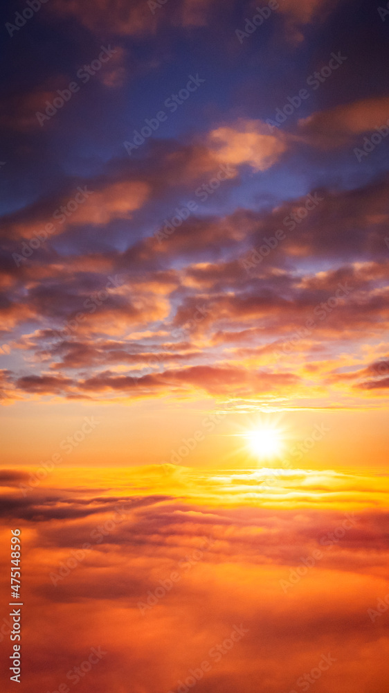 Vertical 9:16 photo of setting sun above the clouds. Beautiful vibrant background of heaven-like sky