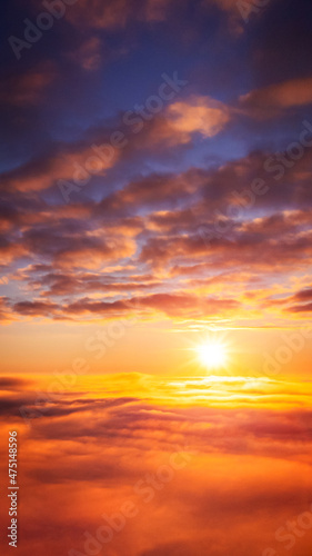 Vertical 9:16 photo of setting sun above the clouds. Beautiful vibrant background of heaven-like sky