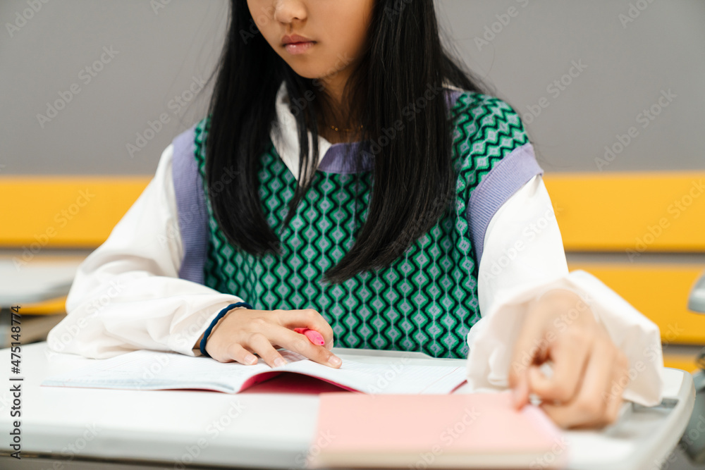 Asian girl writing in exercise book during class in school Asian girl writing in exercise book during class in school