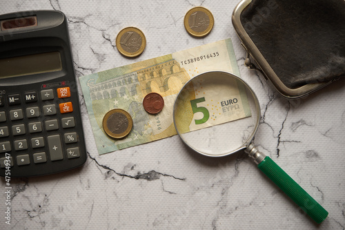banknot o nominale 5 euro ,kilka monet euro ,czarna torebka i kalkulator na marmurze