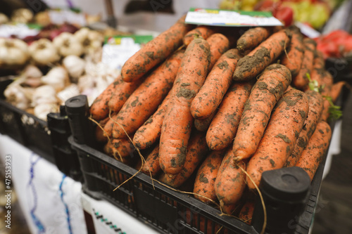Shallow depth of field (selective focus) image with organic fresh carrots covered in soil for sale in an outdoors market in Bucharest, Romania.
