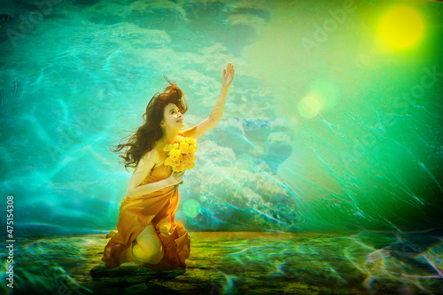 Girl in a beautiful dress under blue water. Female model posing under water in swimming pool