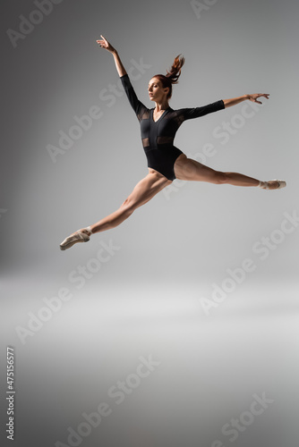 lightweight ballerina in pointe shoes and black bodysuit jumping on dark grey