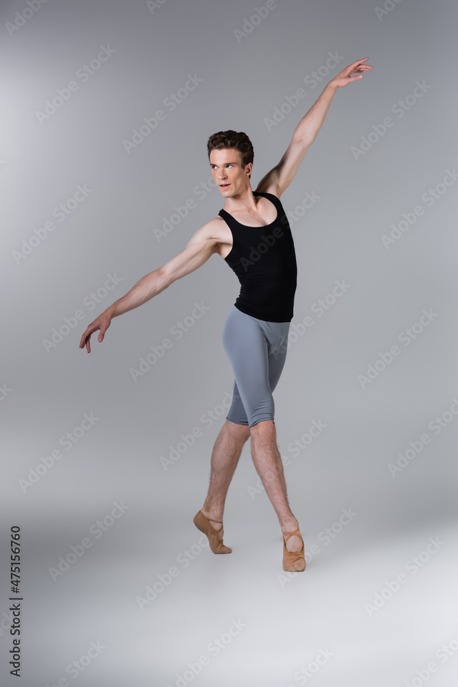 full length of young man in ballet shoes performing ballet dance on grey full length of young man in ballet shoes performing ballet dance on grey