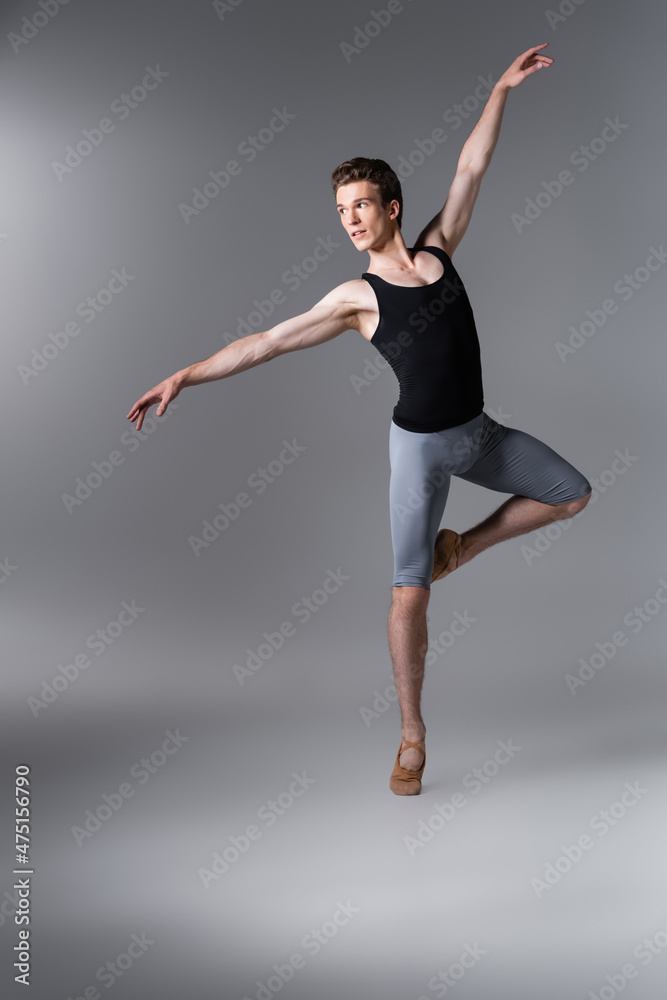 young dancer in tank top gesturing while performing ballet dance on dark grey