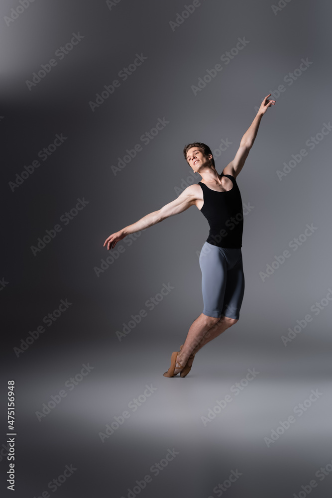 graceful dancer with outstretched hands performing ballet dance on dark grey