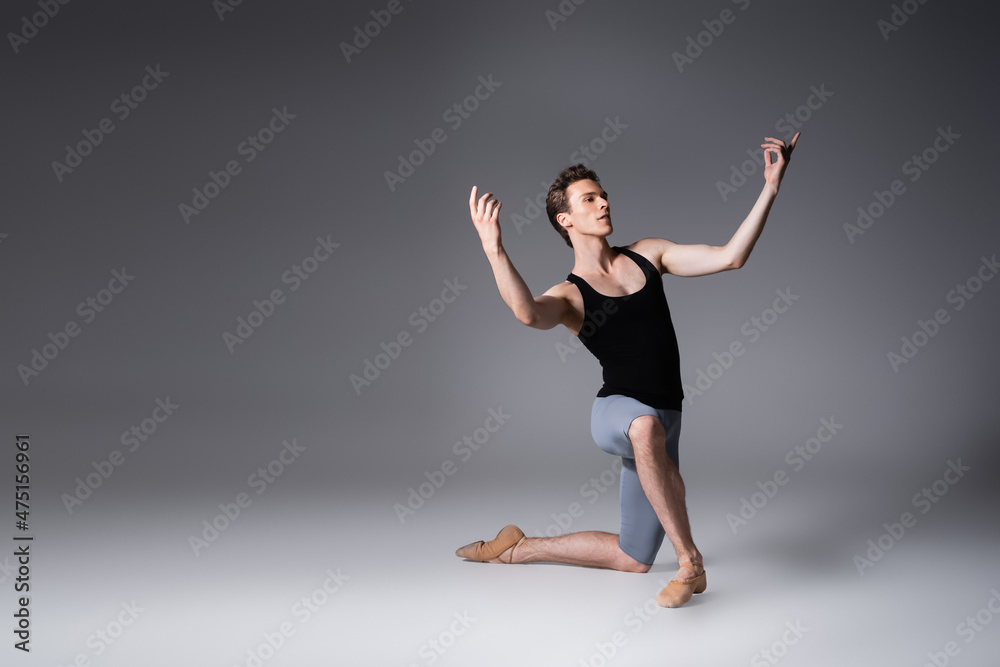 full length of graceful ballet dancer standing on knee while performing ballet dance on dark grey