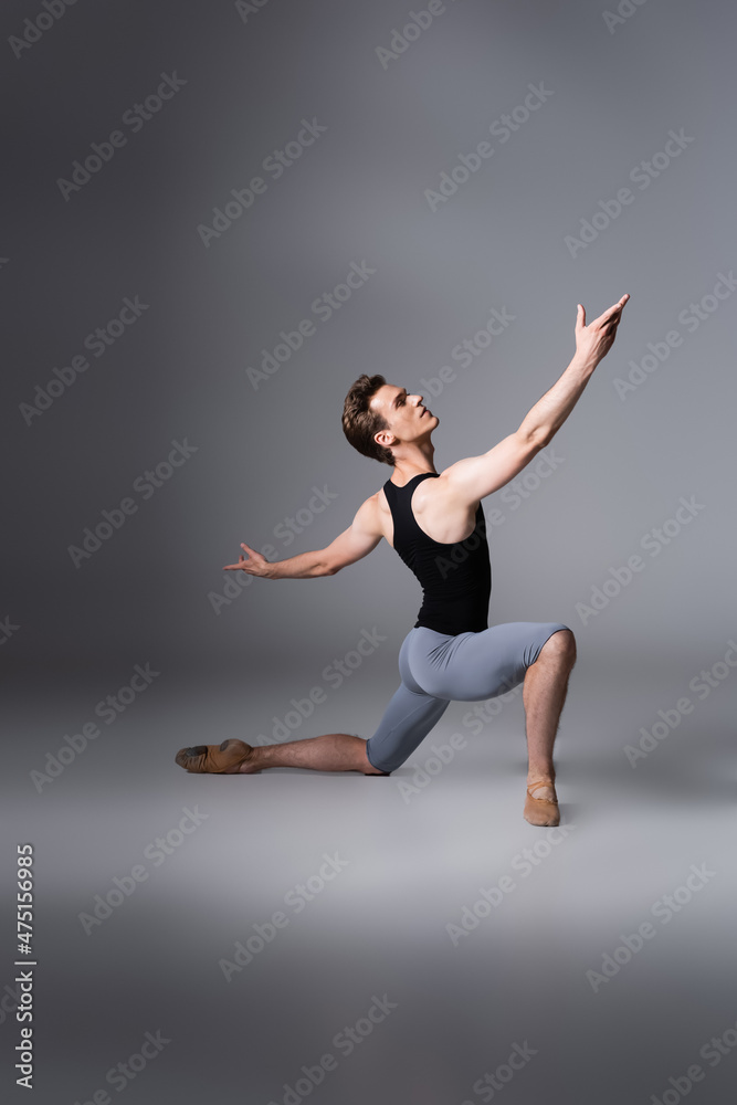 young ballet dancer in black tank top performing ballet dance while standing on knee on dark grey