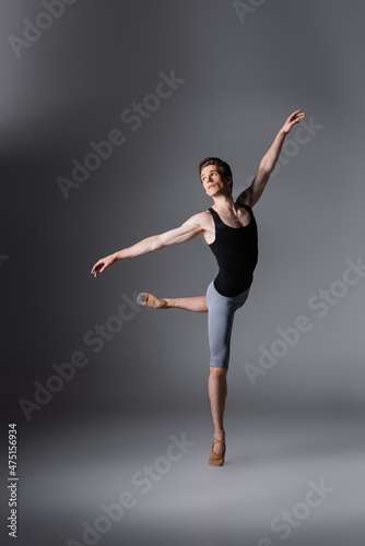 full length of elegant man in ballet shoes performing ballet dance on dark grey