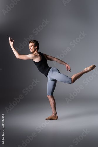 full length of graceful ballet dancer in tank top gesturing on dark grey