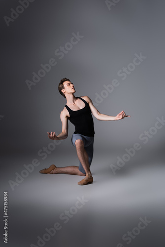 full length of elegant ballet dancer standing on knee while performing ballet dance on dark grey
