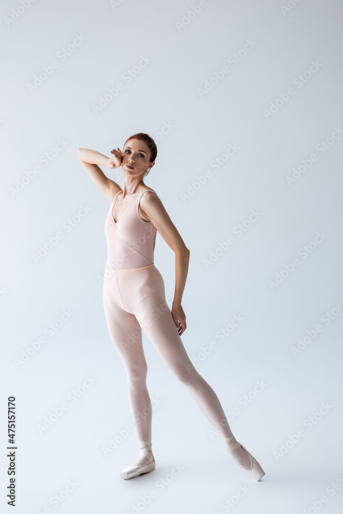 full length of elegant ballerina in bodysuit looking at camera on grey full length of elegant ballerina in bodysuit looking at camera on grey